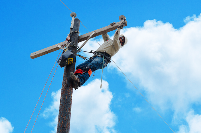 电线工人在检查电线杆上的电线，并将其固定在安全设备上.
